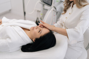 Obraz premium Close-up hands of cosmetologist performing microneedling with mesotherapy serum on woman face in professional clinic, promoting collagen, skin rejuvenation, lifting and glowing anti-aging results.
