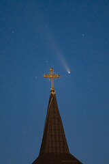 Celestial and Spiritual: Rare Comet ATLAS 2024 Shines Brightly in the Night Sky Behind the Illuminated Cross of an Old Wooden Church, Symbolizing Faith and Science