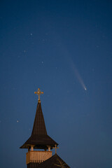 Celestial and Spiritual: Rare Comet ATLAS 2024 Shines Brightly in the Night Sky Behind the Illuminated Cross of an Old Wooden Church, Symbolizing Faith and Science
