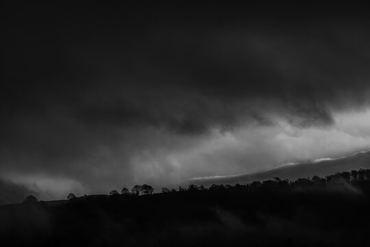 Black and white hillside silhouettes under dramatic cloud