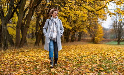 Beautiful middle-aged woman walking in park in autumn scenery. Front view	