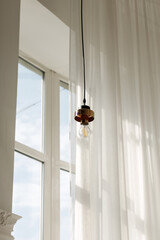Modern hanging light fixture with soft natural light through sheer curtains and large window