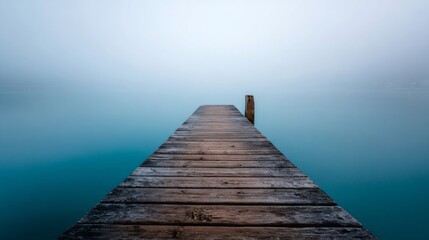 Fototapeta premium Wooden jetty extending into a tranquil, foggy lake water, creating a minimalist concept of peace and solitude