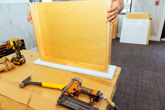 Wood worker is working on assembling wooden drawer frame while using tools at workspace - Powered by Adobe