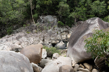 Large grey natural boulders and jagged rocks scattered across a lush green mountain slope under a dense forest canopy.