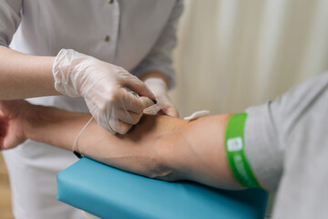 Medical professional in sterile gloves inserts needle into male patient arm vein to collect blood into tube for routine testing, diagnostic laboratory analysis, close-up. Concept of healthy lifestyle