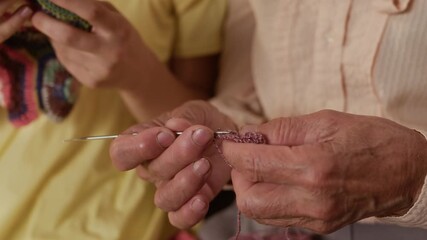 Close up of wrinkled hand of elderly woman knitting scarf with needle while teaching granddaughter crafting technique spending weekend together at home, copy space - Powered by Adobe