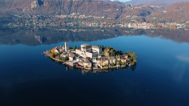 Aerial view of Isola San Giulio island, with its historic buildings casting shadows on the tranquil water, a serene scene of Italian architecture, Isola San Giulio, Piemonte, Italy.