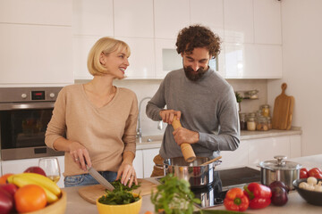 A couple prepares a meal in their stylish kitchen, chopping vegetables and seasoning a pot.