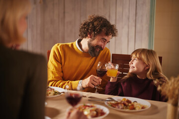 Family members enjoy a warm autumn dinner together, sharing food and drinks, while a father and...