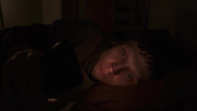 Man doomscrolling at night in dark bedroom, loneliness, insomnia and emotional burnout