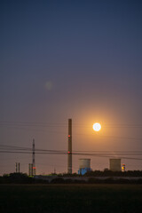 Dramatic Full Moon Rising Between Tall Industrial Chimneys and Cooling Towers at Twilight, Symbolizing Energy, Contrast, and Pollution