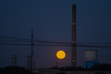 Dramatic Full Moon Rising Between Tall Industrial Chimneys and Cooling Towers at Twilight, Symbolizing Energy, Contrast, and Pollution
