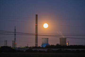 Dramatic Full Moon Rising Between Tall Industrial Chimneys and Cooling Towers at Twilight, Symbolizing Energy, Contrast, and Pollution