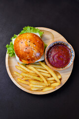 Tasty beef burger with french fries on the wooden plate with red sauce