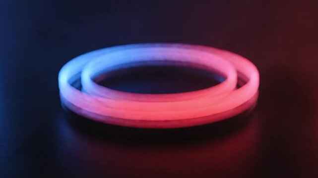 Pulsating red and blue emergency lights spin rapidly, forming luminous, overlapping rings reflected on a dark, glossy surface, strongly evoking the urgency of police or ambulance sirens.