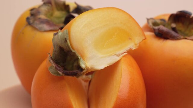 Several persimmons rotate while a juicy slice in front reveals the bright flesh. The macro shot moves smoothly to highlight texture and freshness.