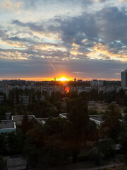 City skyline at sunset with dramatic clouds and golden sunlight. The sun sets over the city, casting a warm glow on the buildings and creating a beautiful sky