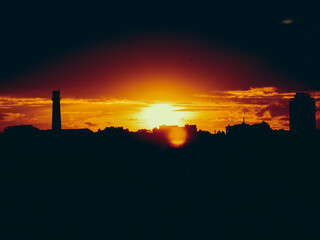 Dramatic sunset over city skyline with silhouetted buildings and fiery sky. The sun sets behind the city, casting a warm glow over the buildings and creating a beautiful silhouette