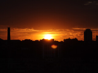 City skyline silhouetted against a vibrant orange sunset. The sun sets behind a city, casting a warm glow over the buildings and creating a dramatic silhouette