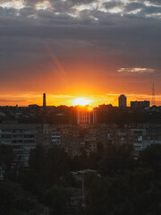 Dramatic sunset over city buildings with a vibrant orange and yellow sky. The sun sets behind the city buildings, casting a warm glow over the landscape and creating a beautiful scene