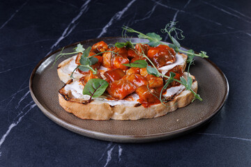 Close-up of tomato bruschetta on artisan bread slices with fresh sliced tomatoes, parmesan cheese and herbs on blue plate, cooking moment. Food preparation process, bruschetta, sandwiches.