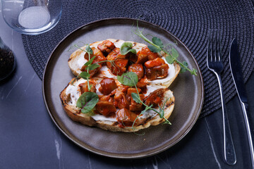 Close-up of tomato bruschetta on artisan bread slices with fresh sliced tomatoes, parmesan cheese and herbs on blue plate, cooking moment. Food preparation process, bruschetta, sandwiches.