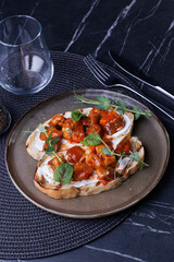 Close-up of tomato bruschetta on artisan bread slices with fresh sliced tomatoes, parmesan cheese and herbs on blue plate, cooking moment. Food preparation process, bruschetta, sandwiches.