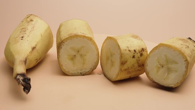 Peeled banana pieces slowly rotate in a neat row on a pastel backdrop. The smooth turntable motion highlights the creamy cross-sections.