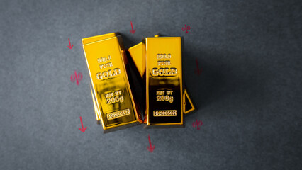 Concept of gold price decrease. Gold bars on a dark background with red arrows pointing down and percentage signs. Financial crisis, recession, or interest rates going down.