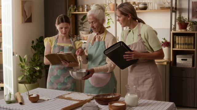 Grandmother in apron mixing ingredients with spoon in bowl teaching young girl and adult daughter biscuits recipe while child writing notes in cozy kitchen, slow motion