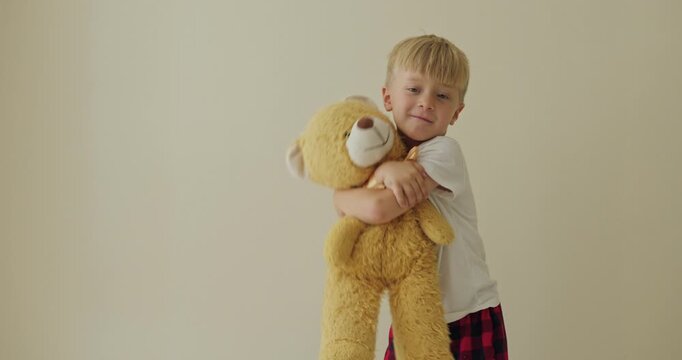 White boy hugging yellow teddy, minimalist beige wall background, red plaid pajama pants, soft plush squeezed close, gentle facial expressions alternating
