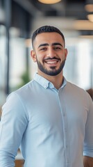 Obraz premium Young Man in Light Blue Shirt Smiling Confidently in a Modern Office Setting During Daytime