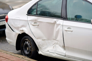 Automobile with broken side panels, dented , damaged rear door and scratched bumper parked on...