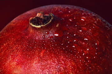 Macro photo of a pomegranate with a red wrinkled skin and a cup decorated with shiny water droplets.