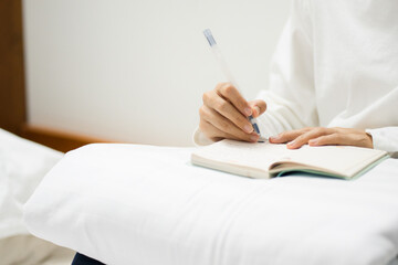 Fototapeta premium Pensive young woman lying on bed with serious expression writing on journal. copy space concept.