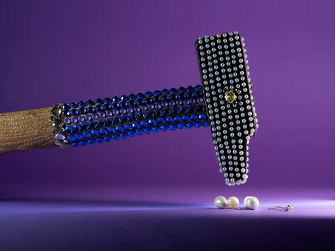 Close-up of a Hammer covered with assorted beads and imitation gemstones about to hit pearls
