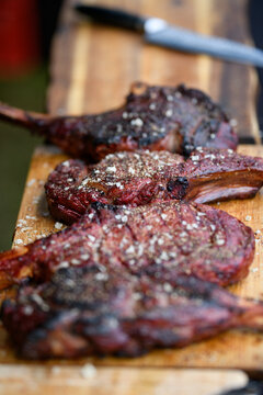 Close-up of four Tomahawk steaks and a knife on a wooden chopping board