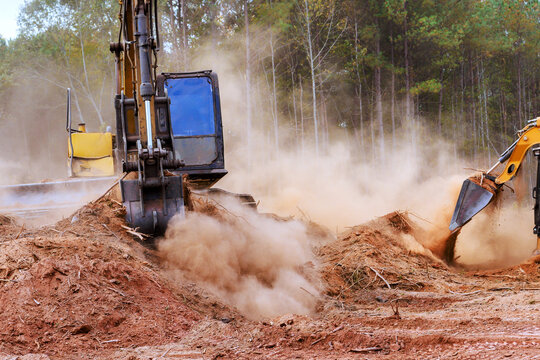 Heavy machines work to clear plot of land, creating dust clouds in forest landscape an active construction area - Powered by Adobe