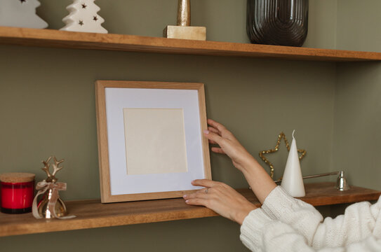 Close-up side view of a Woman's hands arranging an empty picture frame on a shelf amongst assorted festive Christmas decorations