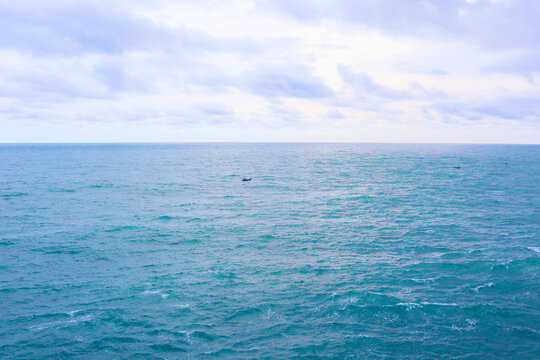 Wide angle seascape of vast turquoise ocean under a dramatic cloudy sky with small distant fishing boats.