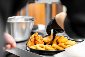 A person wearing black gloves is adding a piece of fried food to a black platter filled with...