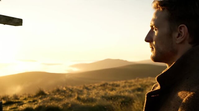 Man watches sunrise by cross. Silhouette profile faces light on hill. Prayer and faith reflected in quiet gaze. Religion symbol stands beside man. Golden landscape and distant ridge frame moment.