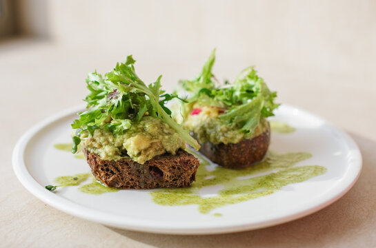Close-up of two slices of brown sourdough toasted bread with avocado and lettuce on a plate