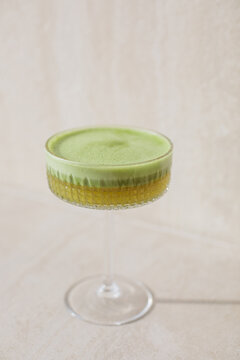 Close-up of a frothy matcha apple drink with plant based milk in an elegant cocktail glass on a beige background