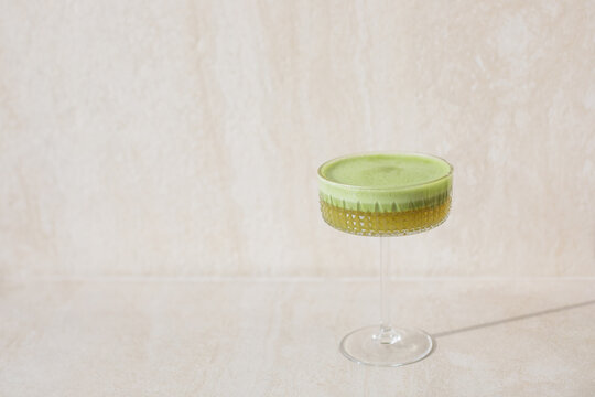 Close-up of a frothy matcha apple drink with plant based milk in an elegant cocktail glass on a beige background