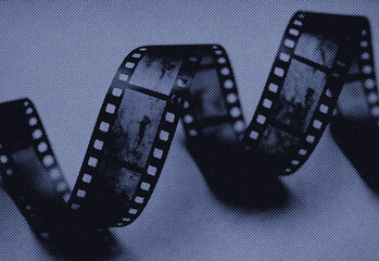 Close up of a vintage film strip curling across a grainy blue background, cinematic reels and perforations hinting at classic movie production, editing, and creative storytelling