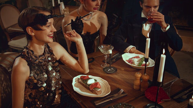 Happy retro friends standing at bar counter with cocktails in warm vintage lighting. Concept of bar social content, festive invitations, nightlife branding materials, themed retro campaigns.