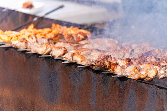 Close-up of rows of pork skewers (shashlik) cooking on an outdoor barbecue