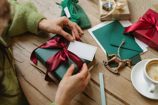Overhead view of a mid adult woman sitting at a table with a cappuccino and a wrapped Christmas gift with a blank gift tag